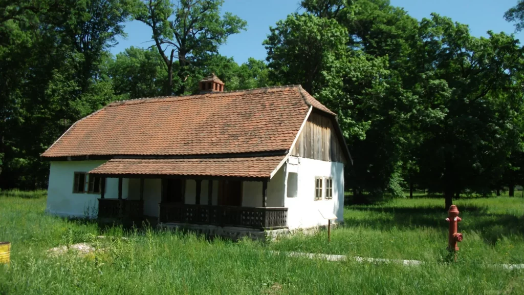 Casă tradițională din chirpici cu pereți albi, acoperiș din țiglă și prispă cu balustradă din lemn