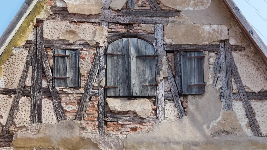 Fronton de casă veche cu structură din lemn și cărămidă, cu tencuiala desprinsă și grinzi degradate